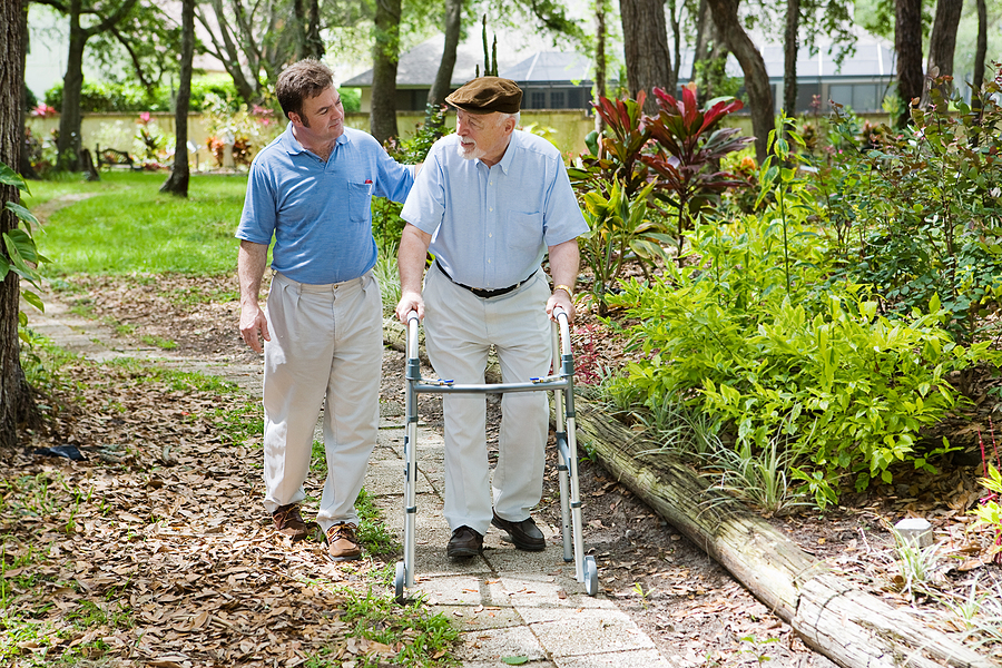 Caregiver walking in garden with elderly man.